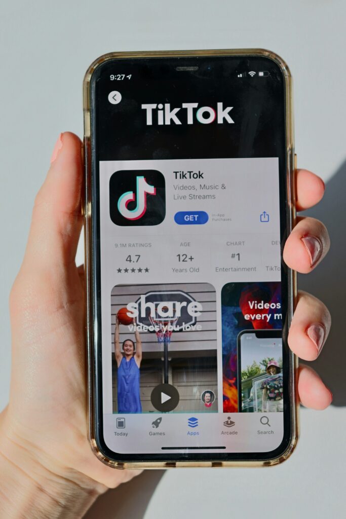 Person holding a smartphone displaying the TikTok app page in the App Store. The app has a 4.7-star rating and is categorized under Entertainment.